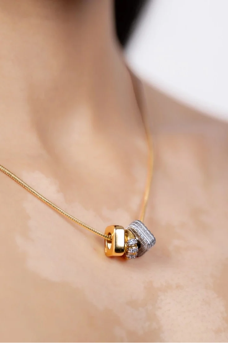 A close-up lifestyle shot of a model wearing a delicate gold chain necklace with a unique interlocking knot pendant featuring gold and silver halves.