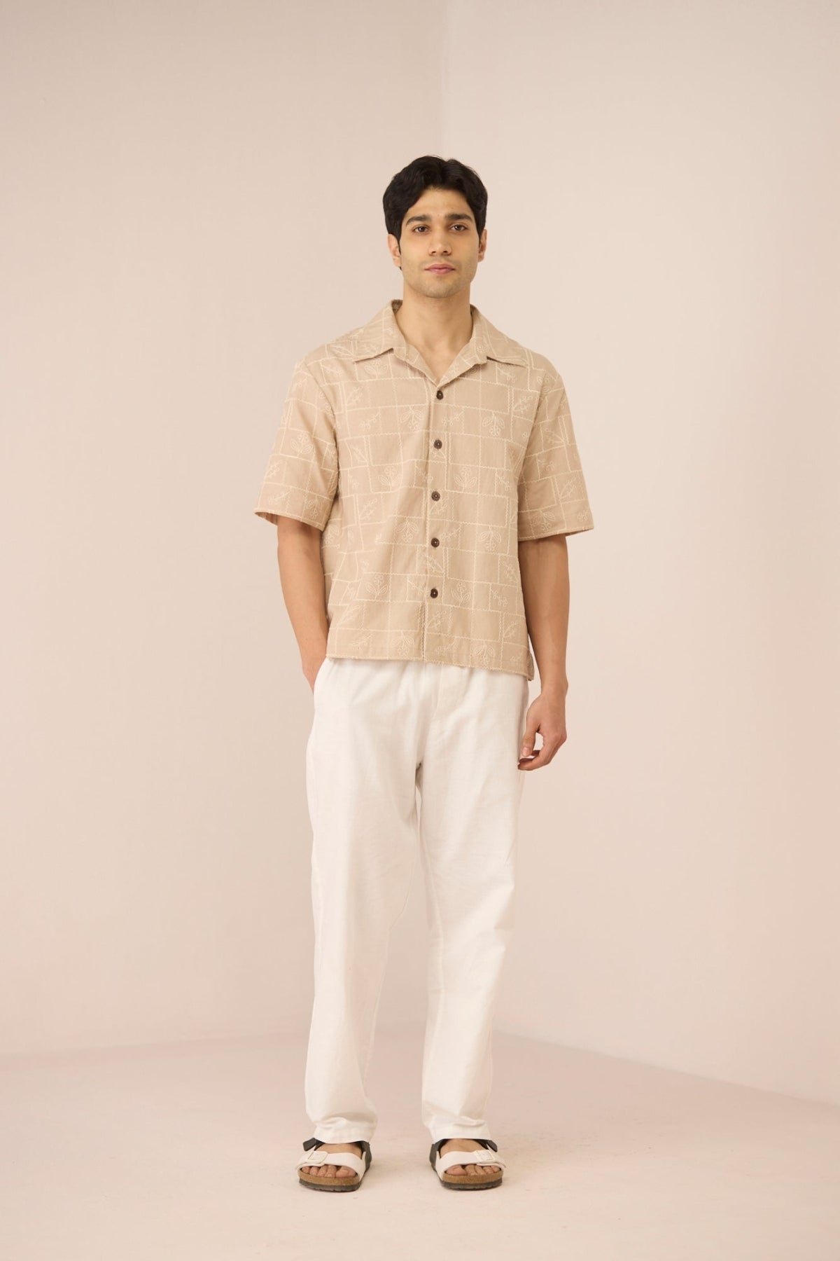 Man wearing a beige shirt and white pants on a plain background Calling June