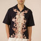 Man wearing a black shirt with pink floral patterns on a beige background Calling June
