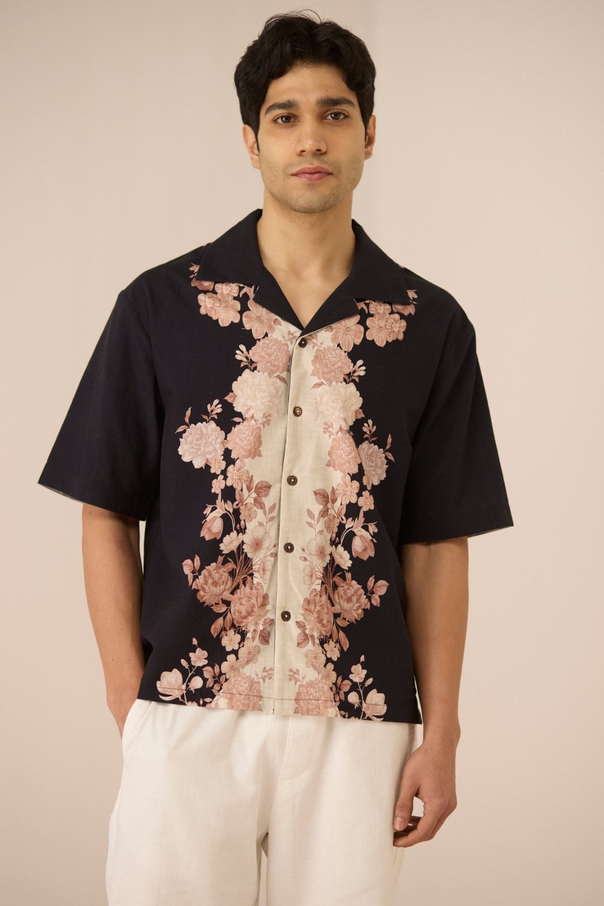 Man wearing a black shirt with pink floral patterns on a beige background Calling June
