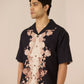 Man wearing a black floral shirt with a beige background Calling June