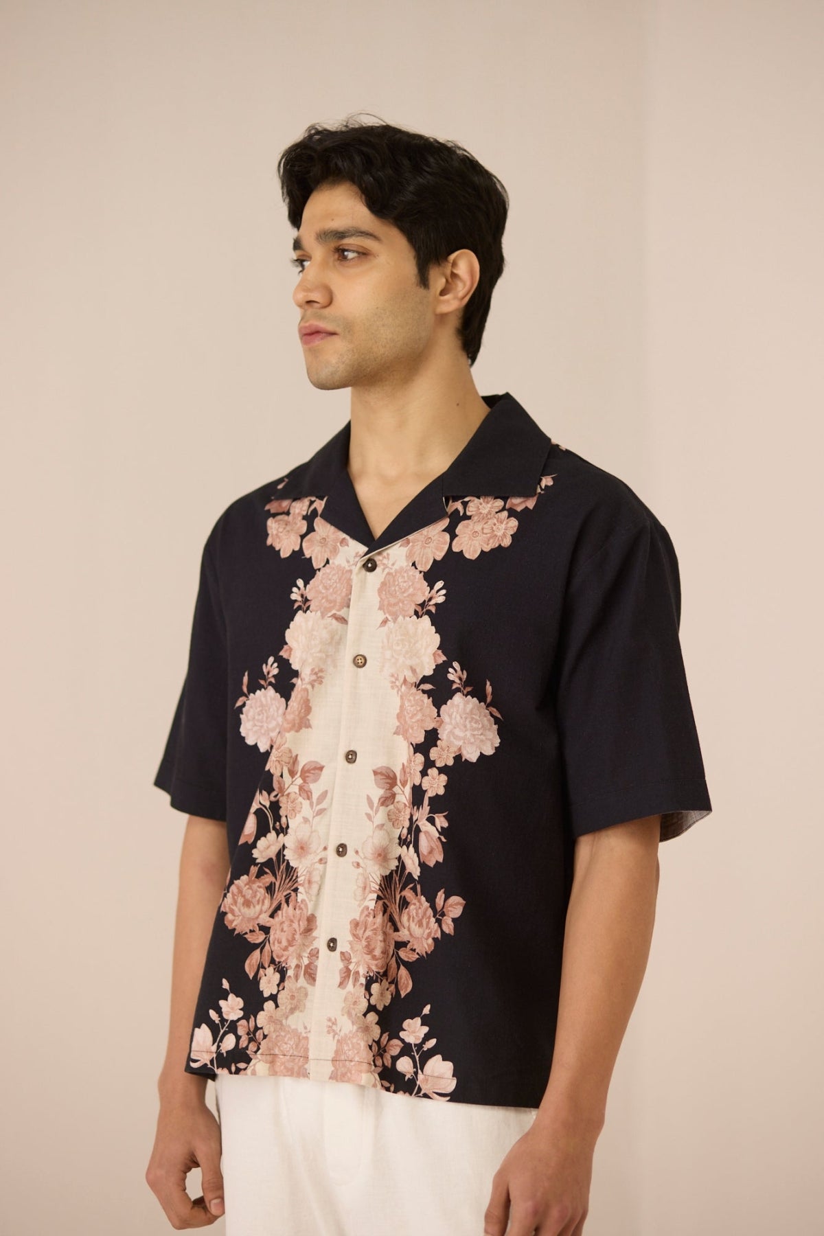 Man wearing a black floral shirt with a beige background Calling June