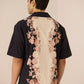 Man wearing a black shirt with floral patterns on a beige background Calling June