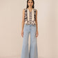 Woman wearing a sleeveless top with floral embroidery and light blue jeans on a beige background Calling June