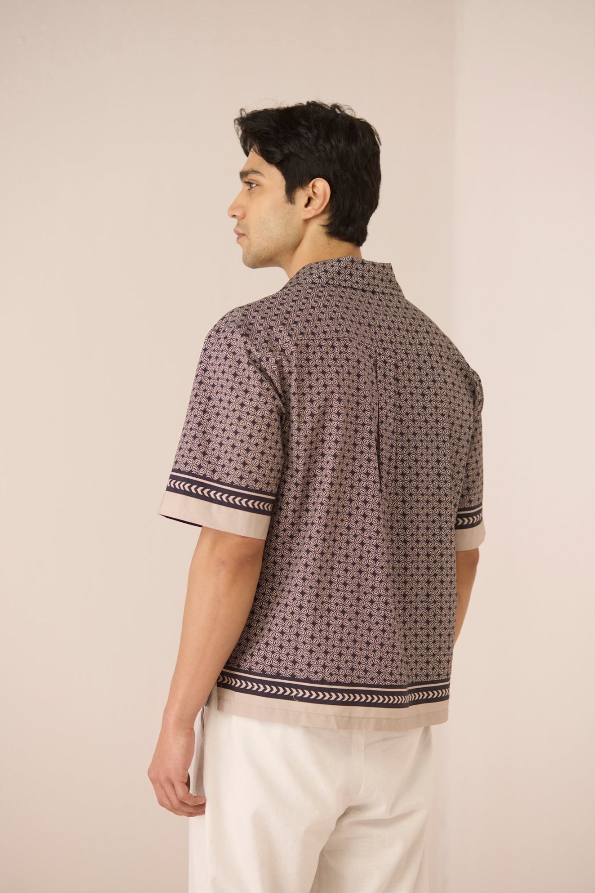 Man wearing a patterned shirt and white pants against a plain background Calling June