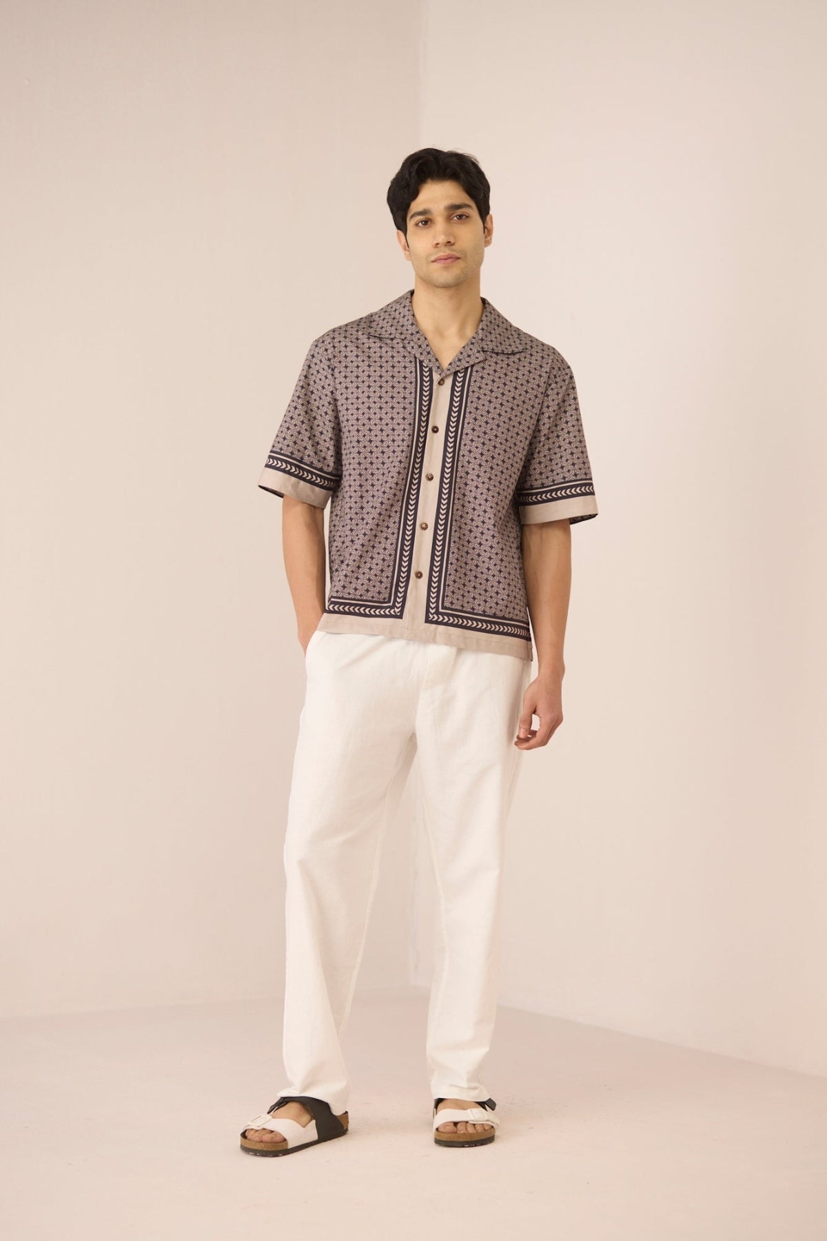 Man wearing a patterned short-sleeve shirt and white pants on a plain background Calling June