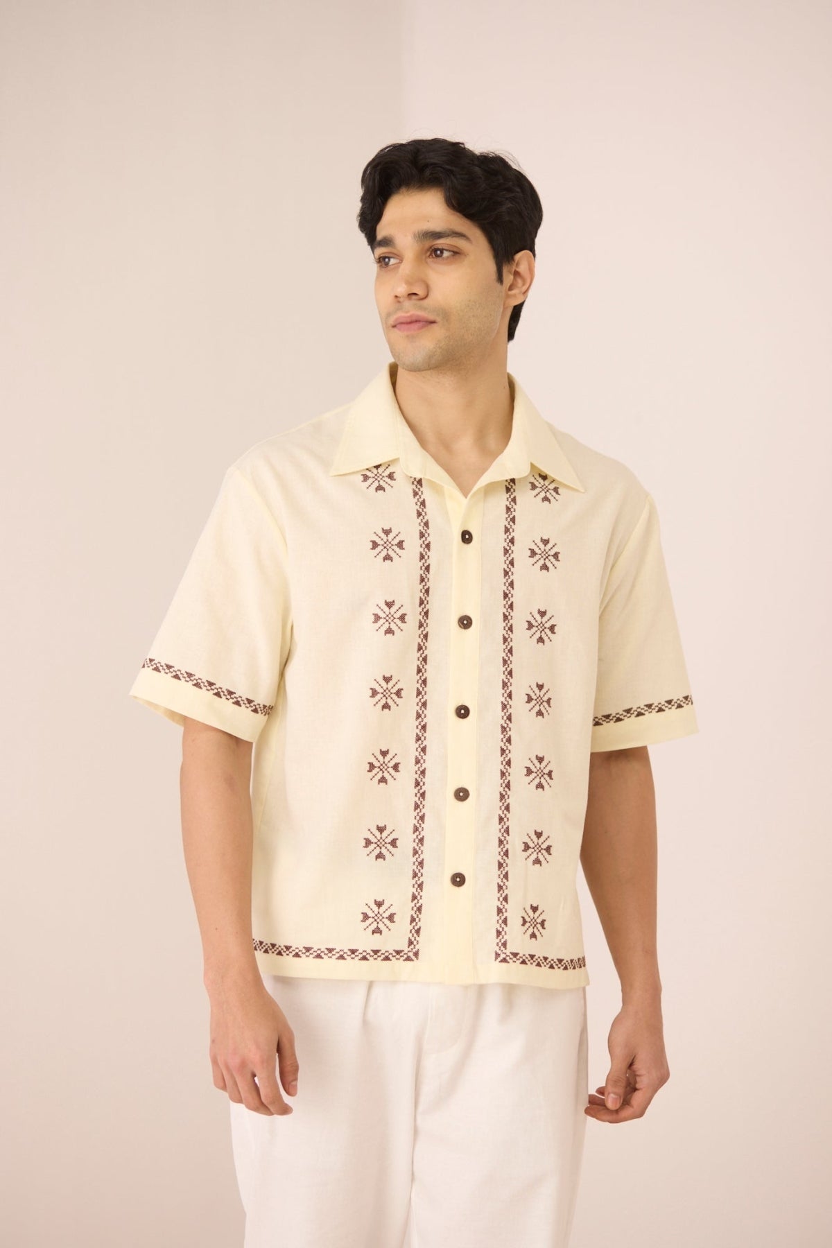 Man wearing a cream-colored embroidered shirt against a plain background Calling June