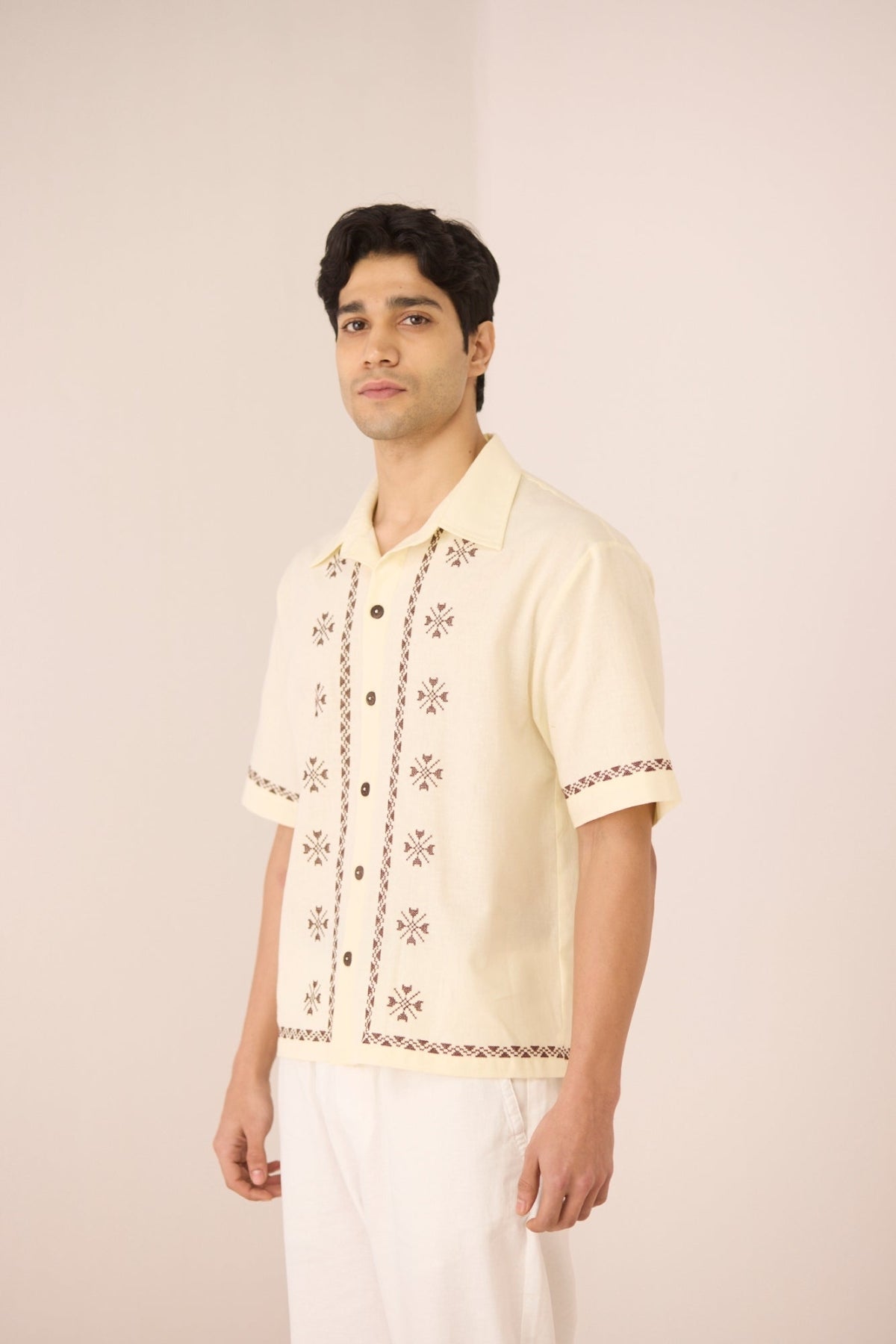 Man wearing a cream-colored embroidered shirt against a plain background Calling June