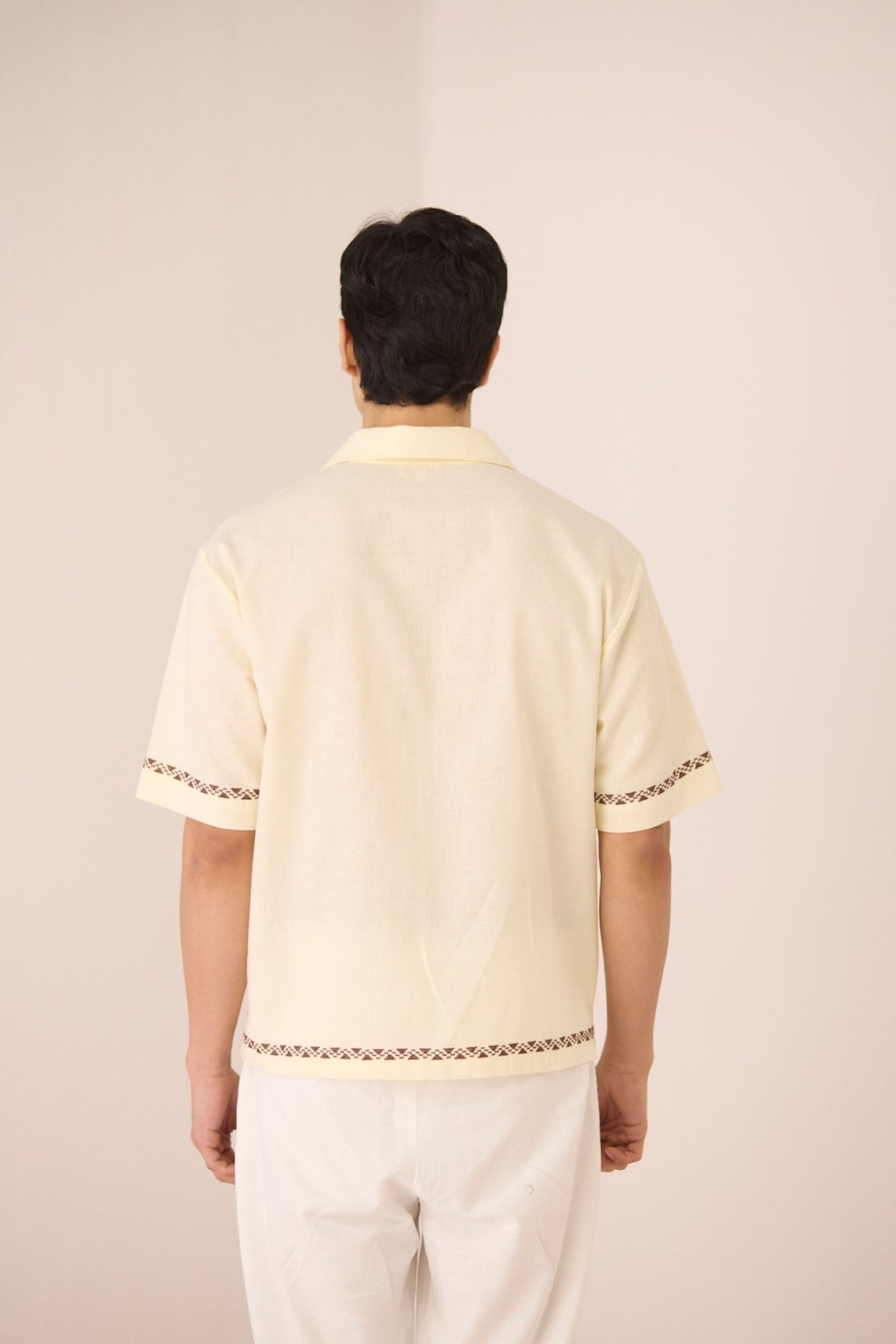 Person wearing a light-colored traditional outfit with intricate designs on a plain background Calling June