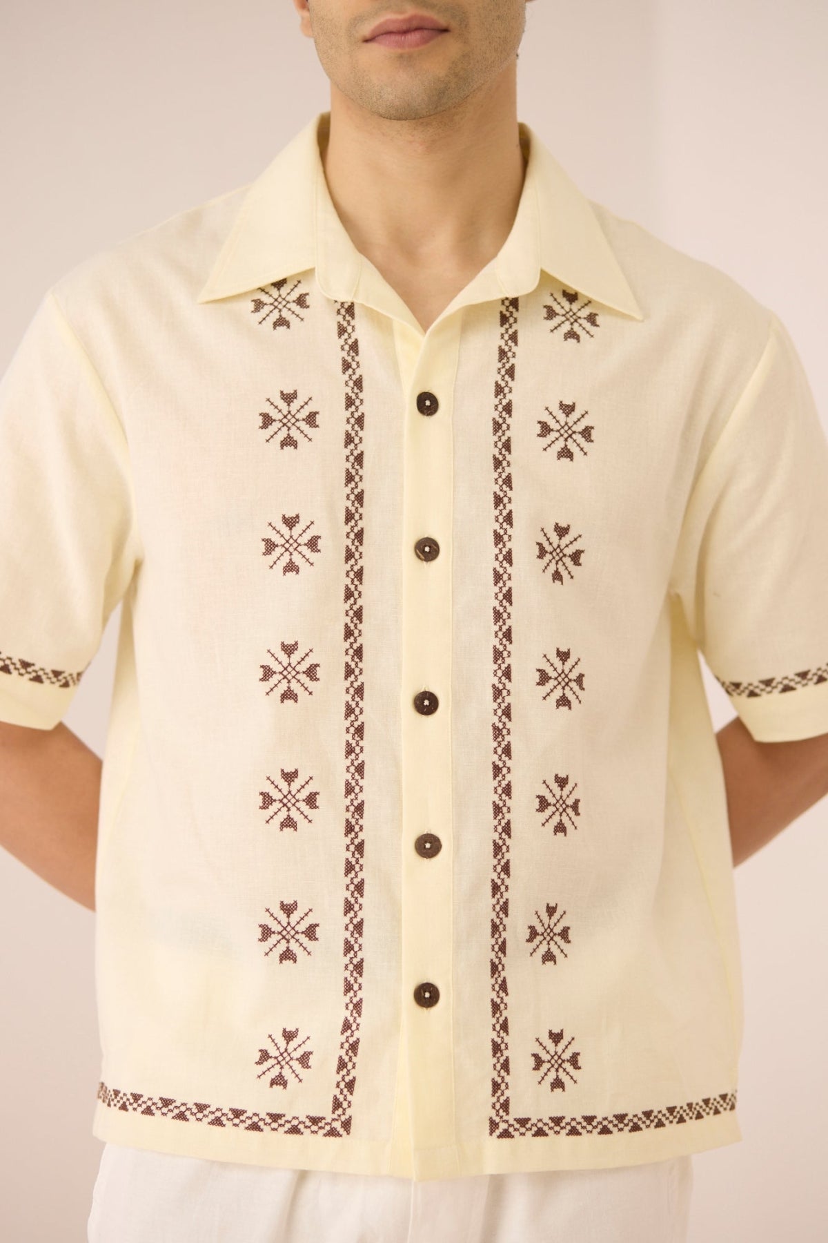 Man wearing a light yellow shirt with black embroidery on a plain background Calling June