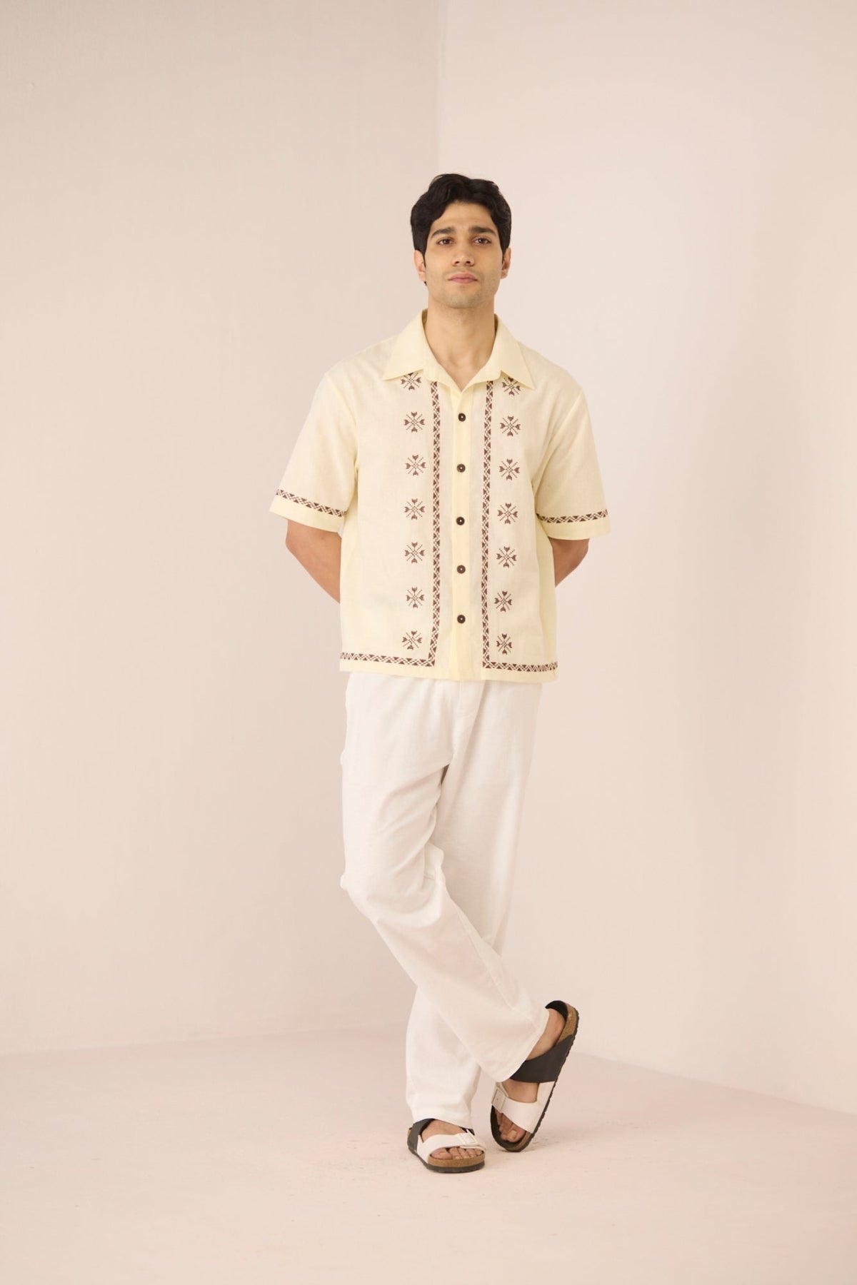 Man wearing a cream embroidered shirt and white pants on a beige background Calling June