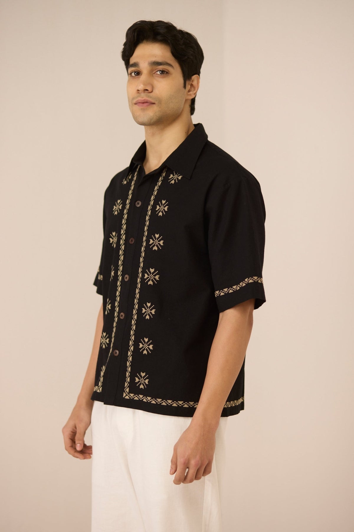 Man wearing a black embroidered shirt with white pants on a beige background Calling June