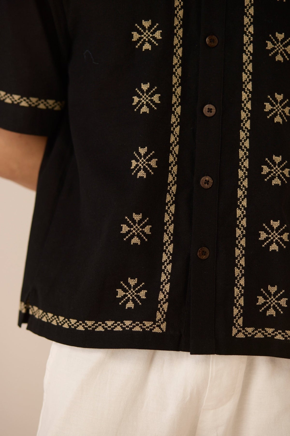Black embroidered shirt with beige patterns on a neutral background Calling June