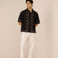 Man wearing a black embroidered shirt and white pants on a beige background Calling June