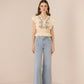 Woman wearing a beige embroidered top and light blue jeans on a beige background Calling June