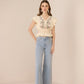 Woman wearing a beige embroidered top and light blue jeans on a beige background Calling June