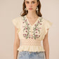 Woman wearing a beige top with floral embroidery and light blue jeans against a beige background Calling June