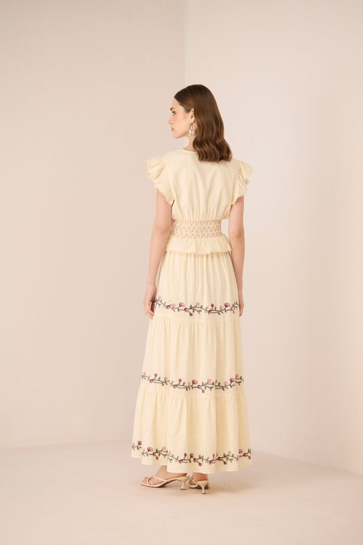 Woman wearing a light yellow set with floral embroidery on a beige background Calling June