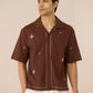 Man wearing a brown embroidered shirt against a beige background Calling June