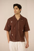 Man wearing a brown embroidered shirt against a beige background Calling June