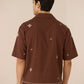 Man wearing a brown embroidered shirt against a beige background Calling June