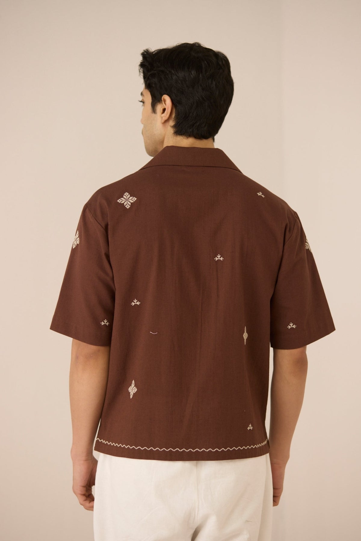 Man wearing a brown embroidered shirt against a beige background Calling June