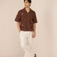 Man wearing a brown short-sleeve shirt with white pants on a beige background Calling June
