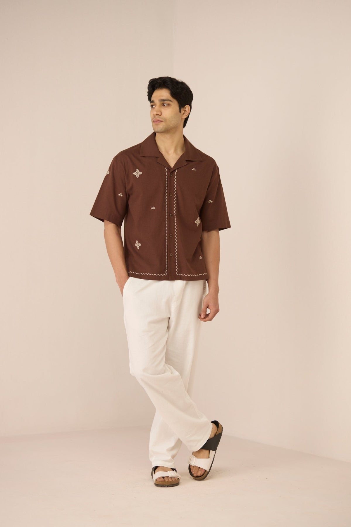 Man wearing a brown short-sleeve shirt with white pants on a beige background Calling June
