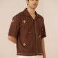Man wearing a brown embroidered shirt against a beige background Calling June