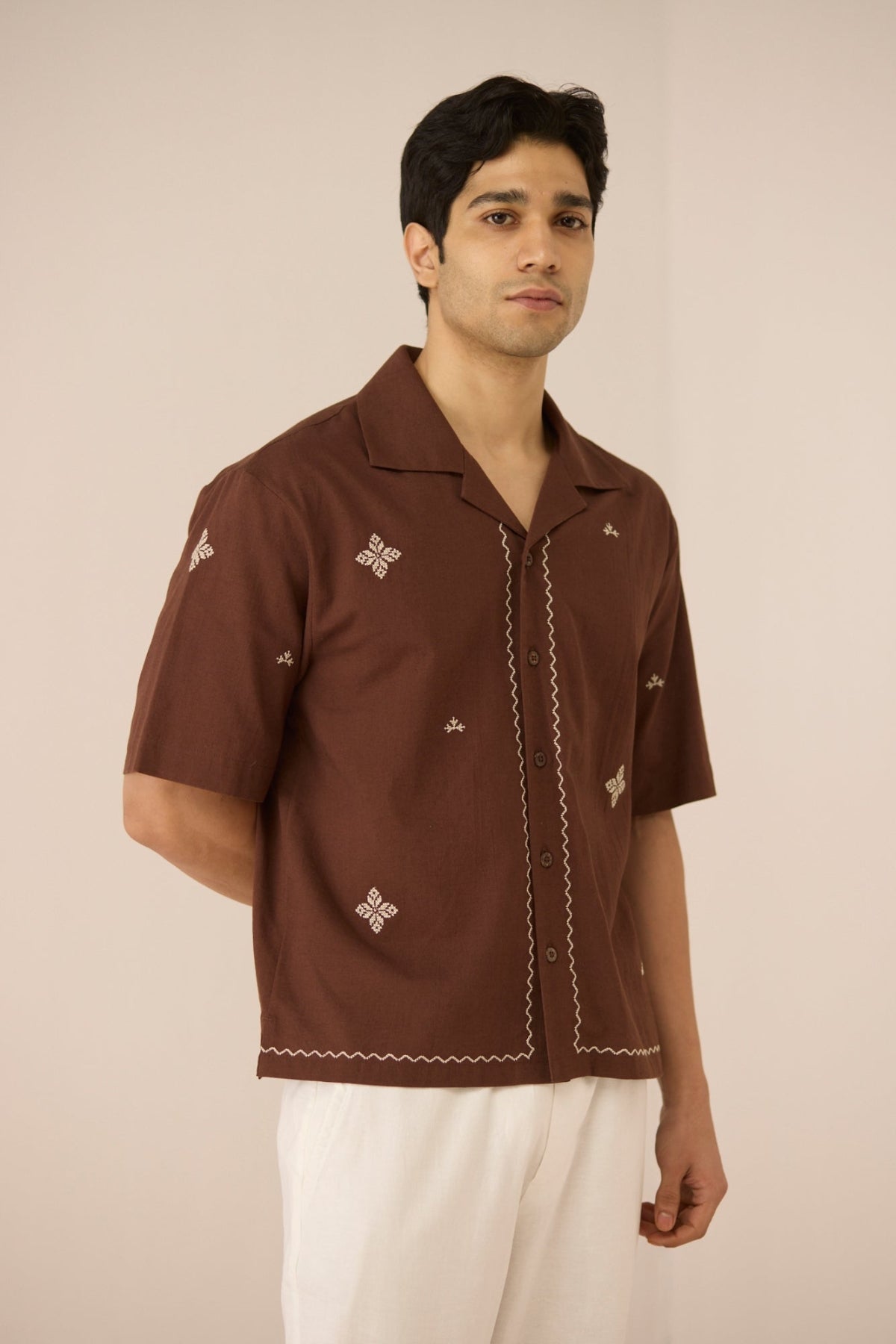 Man wearing a brown embroidered shirt against a beige background Calling June