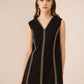 Black dress with gold trim worn by a model on a beige background Calling June