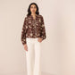 Woman wearing a patterned blouse and white pants against a plain background Calling June