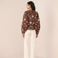 Woman wearing a brown floral blouse and white pants against a beige background Calling June