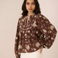 Woman wearing a brown floral blouse against a plain background Calling June