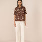 Woman wearing a brown floral blouse and white pants on a beige background Calling June