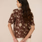 Woman wearing a brown floral blouse against a beige background Calling June