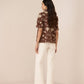 Woman wearing a brown floral blouse and white pants on a beige background Calling June