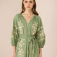 Woman wearing a green embroidered dress against a beige background Calling June