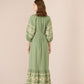 Woman wearing a green dress with floral embroidery on a beige background Calling June