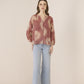 Woman wearing a patterned blouse and light blue pants on a beige background Calling June