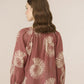 Woman wearing a rust-colored blouse with beige floral patterns on a plain background Calling June