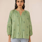 Woman wearing a green embroidered blouse against a beige background Calling June