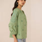 Woman wearing a green embroidered blouse against a beige background Calling June
