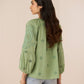 Woman wearing a green embroidered top with light blue jeans on a beige background Calling June