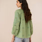 Woman wearing a green embroidered blouse with light blue jeans on a beige background Calling June