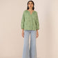 Woman wearing a green embroidered blouse and light blue jeans on a beige background Calling June