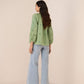 Woman wearing a green embroidered top and light blue jeans on a beige background Calling June