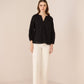 Woman wearing a black blouse and white pants on a beige background Calling June