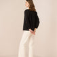 Woman wearing a black jacket and white pants against a beige background Calling June