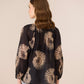 Woman wearing a black blouse with gold floral patterns on a beige background Calling June
